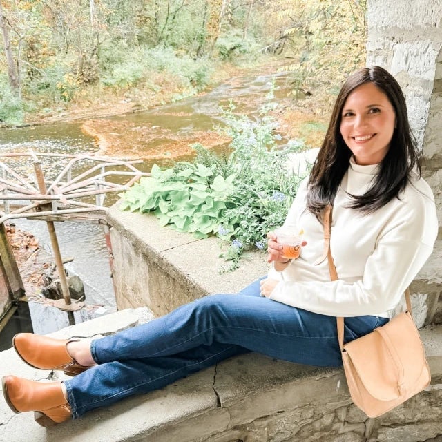 Picture of Kacey in white sweater sitting on a wall in front of a garden