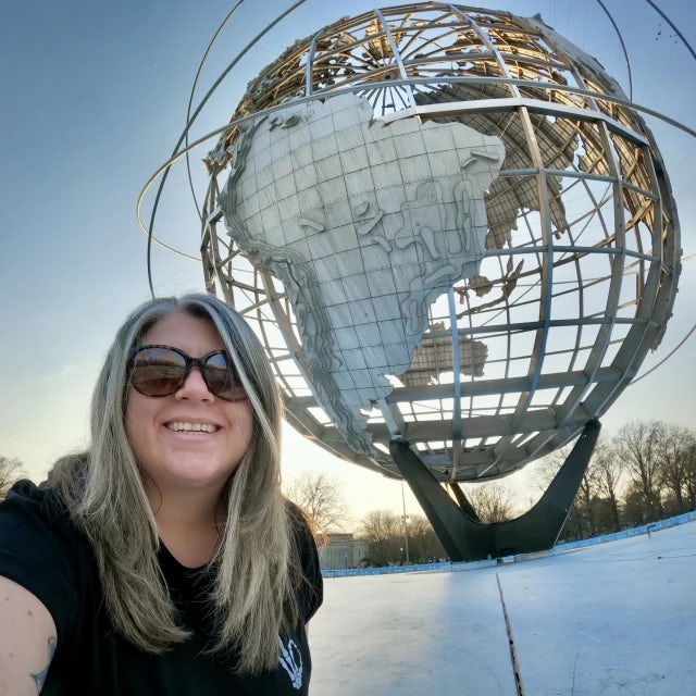 Travel advisor Lauren Powers in a black top posing in front of a large globe structure